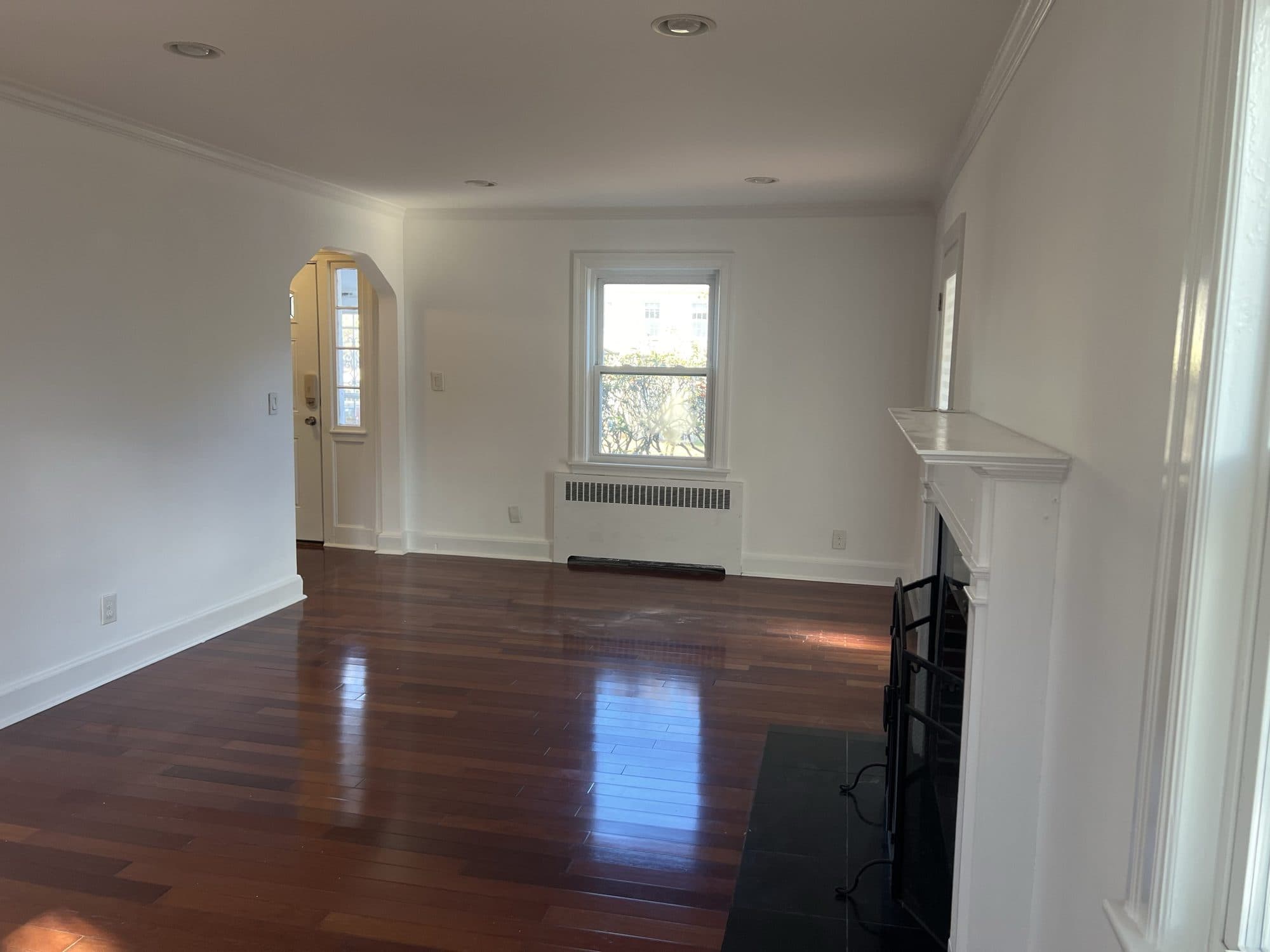Empty living room with cherry floors and a painted fireplace